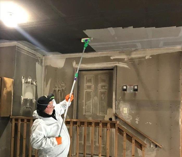 Technician in Personal Protective Equipment using a dry sponge to remove soot from ceiling.
